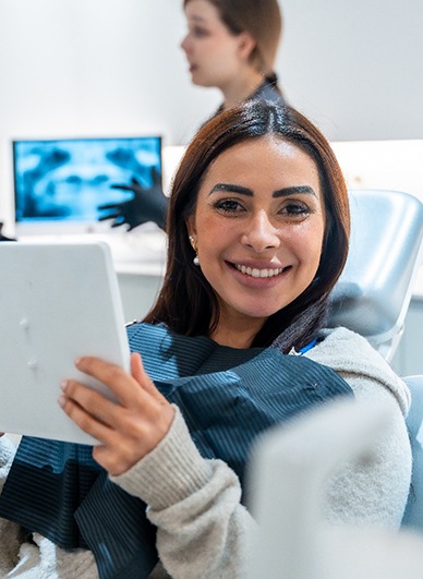 Patient smiling while holding mirror in treatment chair
