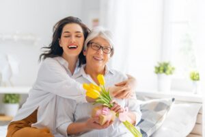 Young mother posing with older mother, holding flowers and a gift. 